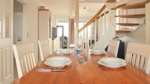 A dining area with a wooden table set for six, white chairs, and a staircase with wooden railings. - liebevoll eingerichtetes Apartement (Rechlin)