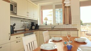 A modern kitchen with white cabinets, a wooden dining table set with plates and cutlery, and a view of a balcony through the window. - liebevoll eingerichtetes Apartement (Rechlin)
