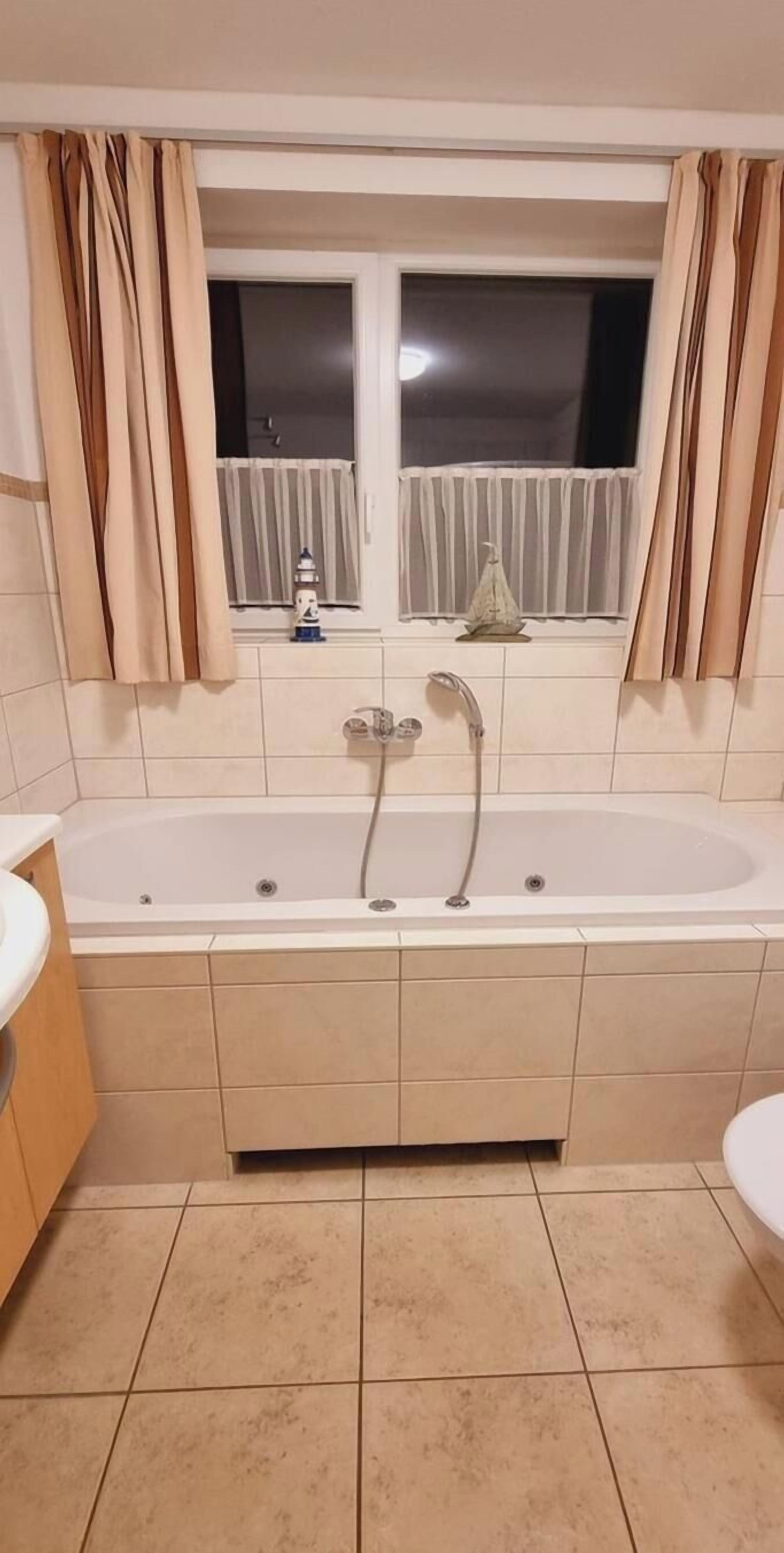 Un baño con una bañera grande, una ventana con cortinas y un lavamanos.