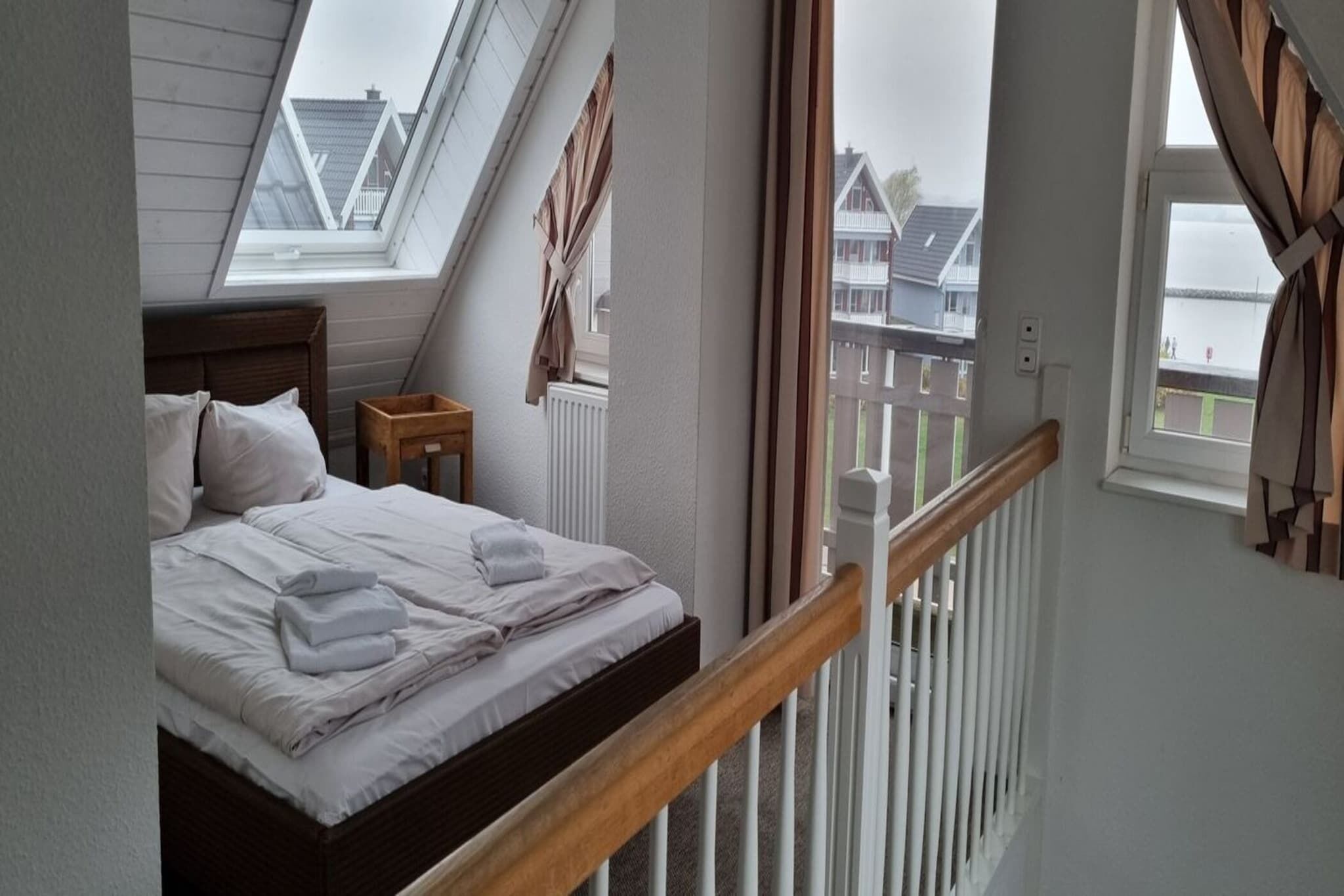 A bedroom with a bed, a nightstand, a window with curtains, and a view of buildings outside.