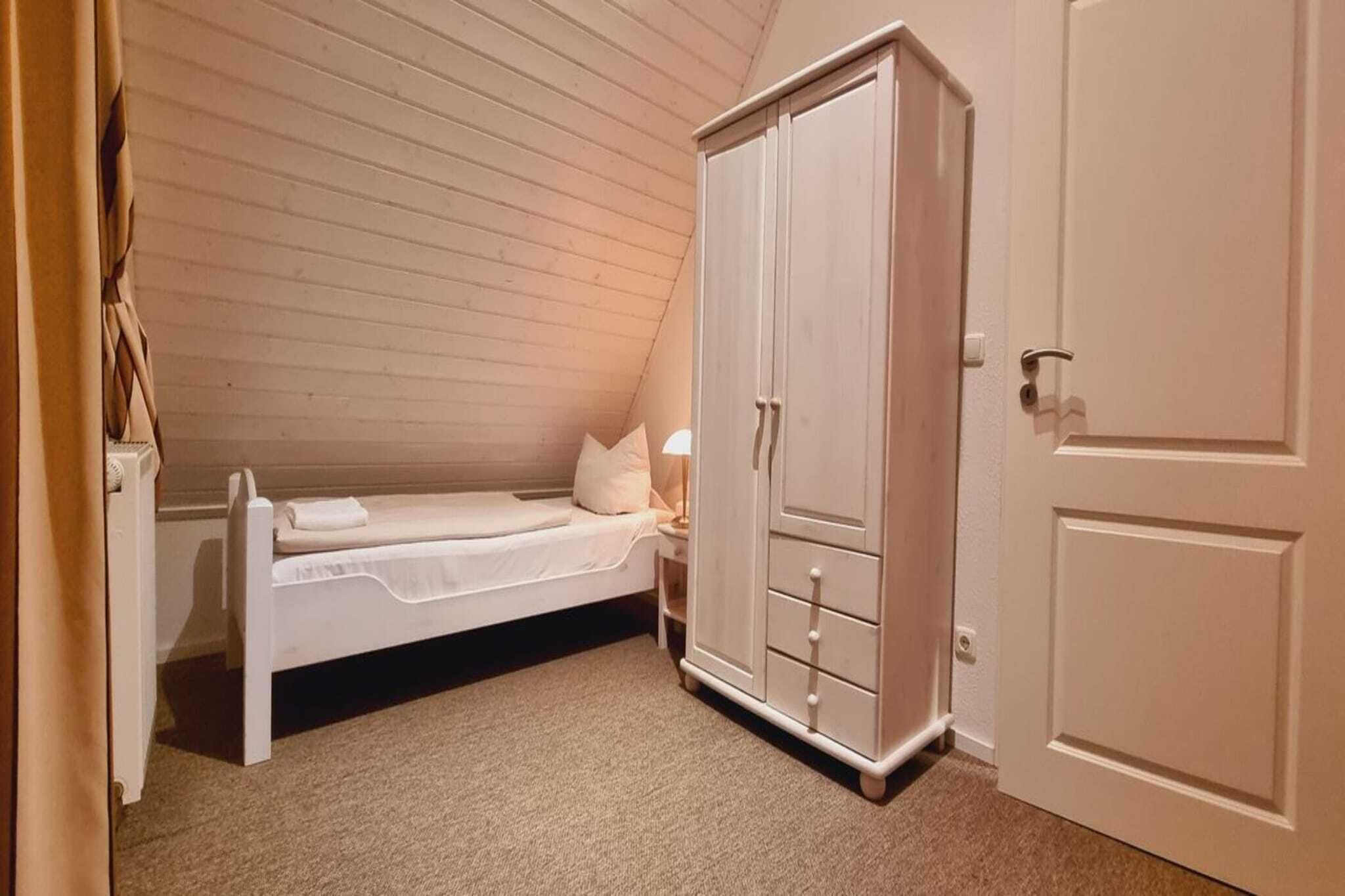 Een kleine kamer met een enkel bed, een witte garderobe en een deur.