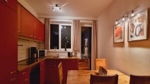 Cuina compacta amb armaris vermells, taula de dinar de fusta i finestra amb cortines.