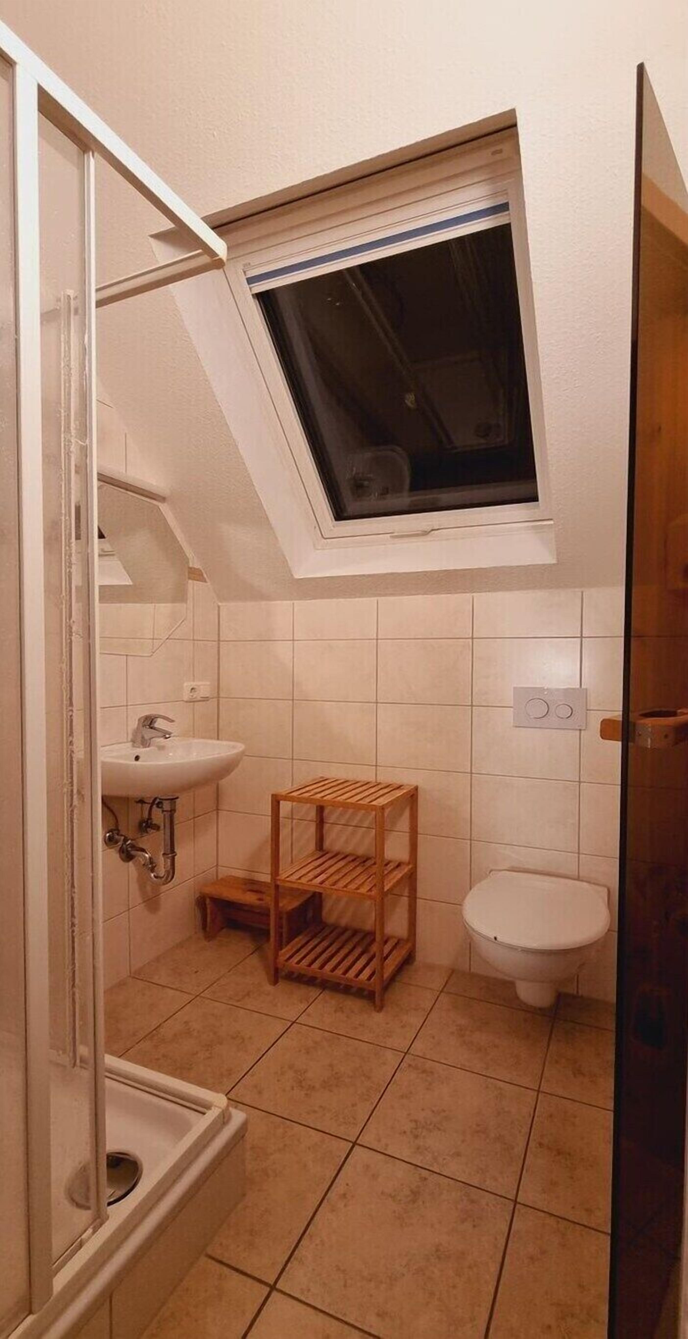 Une petite salle de bain compacte, dotée d’un puits de lumière, d’un lavabo, de toilettes et d’une étagère en bois.