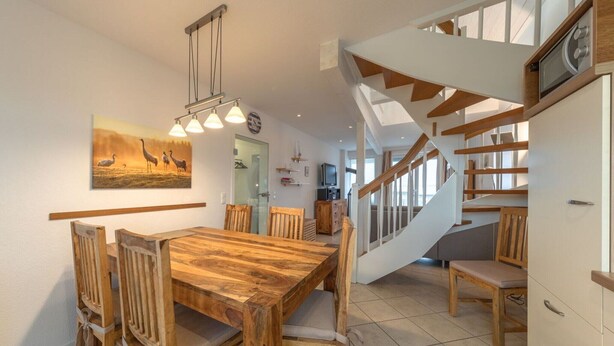 Un coin repas avec une table et des chaises en bois, un tableau au mur et un escalier menant à un autre niveau.