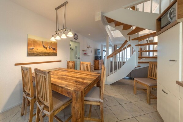 A dining area with a wooden table and chairs, a painting on the wall, and a staircase leading to another level.