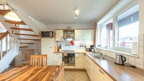 Une cuisine moderne avec une table à manger en bois, un four encastré et une grande fenêtre offrant une vue sur l’extérieur.