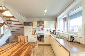 A modern kitchen with a wooden dining table, a built-in oven, and a large window providing a view of the outside. - exklusives Appartement in Rechlin (Rechlin)