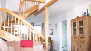 A wooden staircase leading to a loft bedroom, a wooden cabinet with glass doors, and a beige sofa with a red throw pillow. - liebevoll eingerichtetes Appartement (Rechlin)