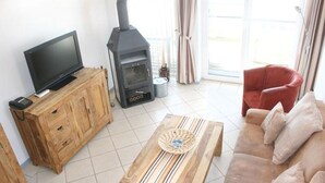 A living room with a TV on a wooden cabinet, a wood-burning stove, a striped table, and a sofa. - liebevoll eingerichtetes Appartement (Rechlin)