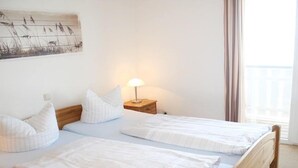 A bedroom with two beds, a nightstand with a lamp, and a window with curtains. - liebevoll eingerichtetes Appartement (Rechlin)