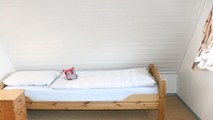 Une petite chambre avec un lit simple, un cadre en bois, du linge de lit blanc et une petite table de chevet en bois.