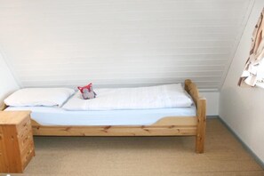 Ein kleines Zimmer mit einem Einzelbett, Holzrahmen, weißer Bettwäsche und einem kleinen Nachttisch.