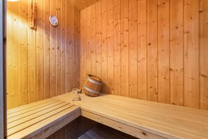 Un sauna avec des murs en bois, un banc, un thermomètre et un seau en bois.