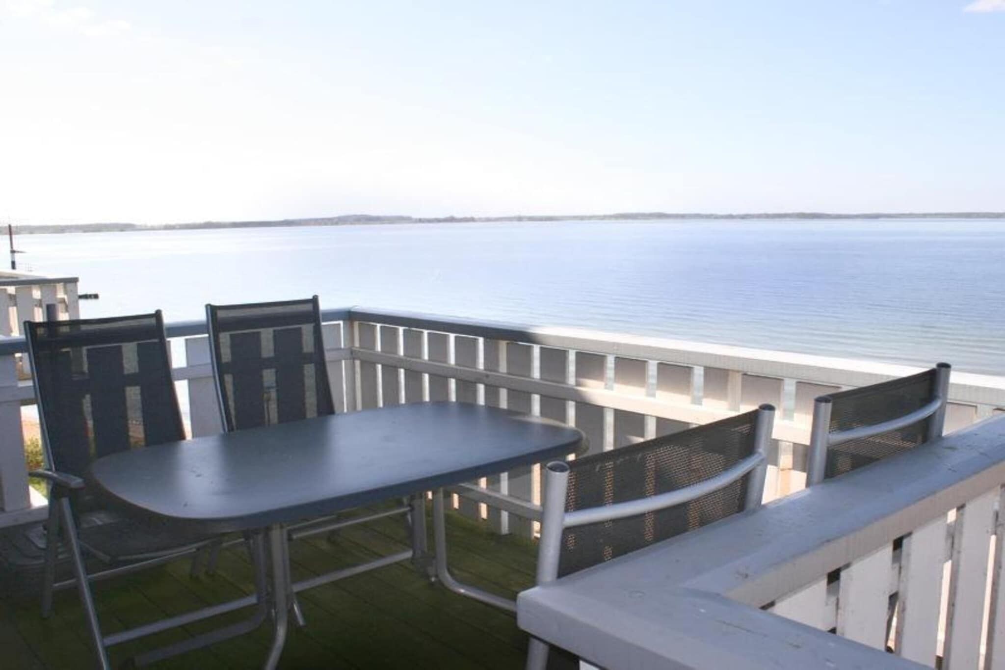 A balcony with a table and chairs overlooking a calm body of water.
