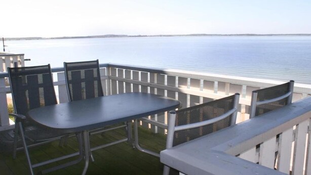 Un balcon avec une table et des chaises donnant sur une étendue d’eau paisible.