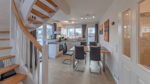 Une cuisine moderne dotée d’un îlot central, d’un escalier en bois et d’un coin repas avec des chaises.