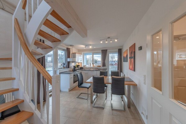 Una cocina moderna con una isla central, una escalera de madera y un comedor con sillas.