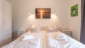 A double bed with white linens, two bedside tables, a nightstand, a wall-mounted painting of a sunset, and a green artwork on the wall. - liebevoll eingerichtetes Appartement (Rechlin)