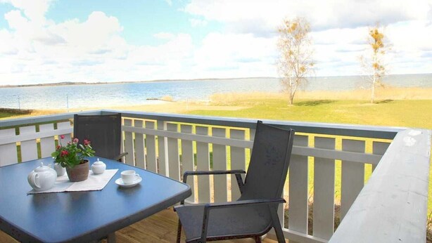 Une terrasse avec une table dressée pour le thé, donnant sur une pelouse et un plan d’eau.