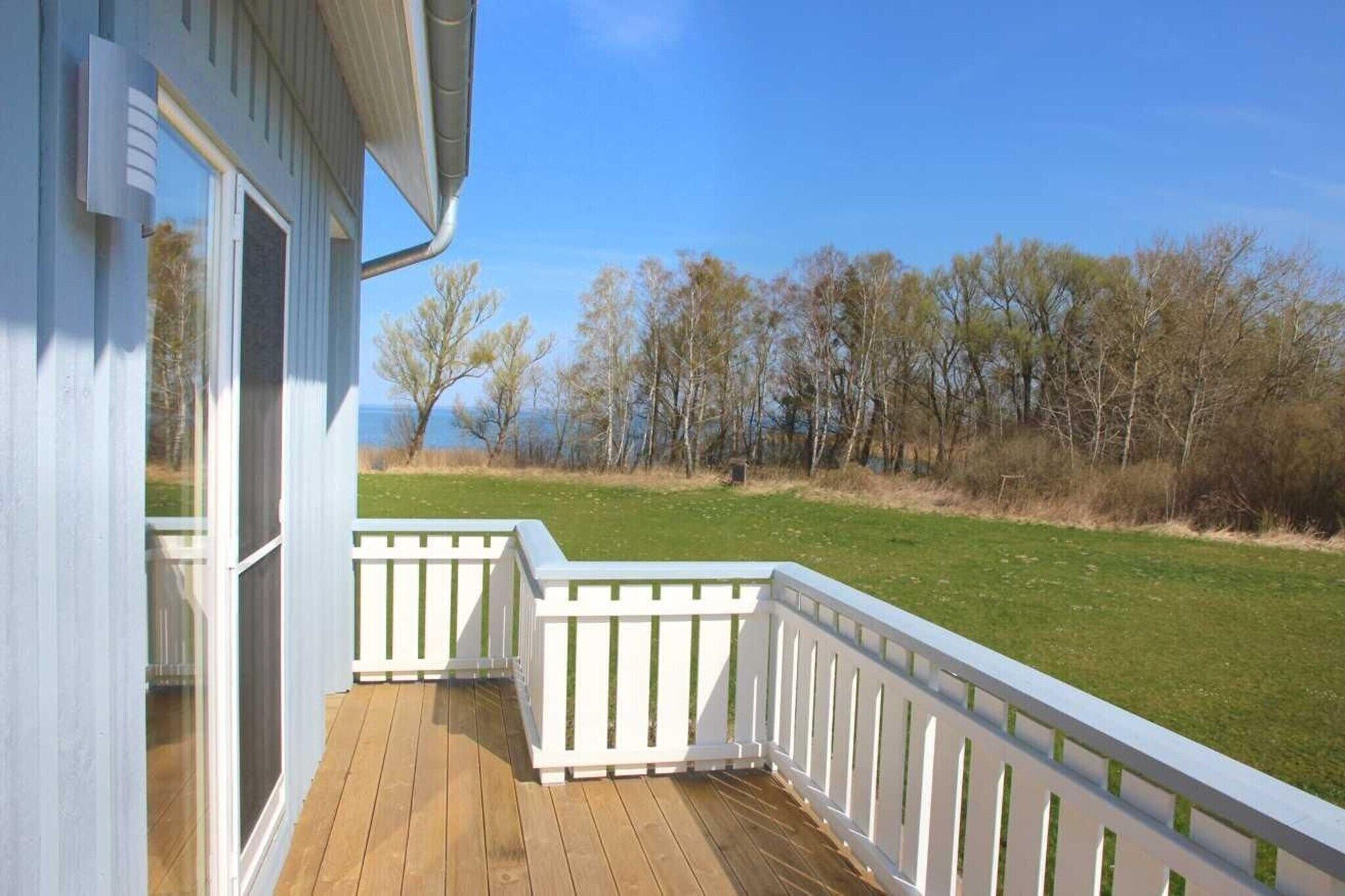 A wooden deck with white railings, a clear view of a grassy area and trees, and a building with large windows.