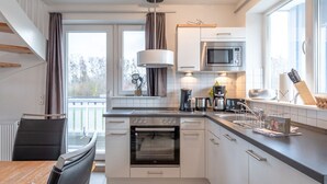 A modern kitchen with white cabinets, a built-in oven, a microwave, and a dining area with a table and chairs. - liebevoll eingerichtetes Appartement (Rechlin)