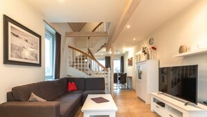 A modern living room with a sofa, coffee table, TV, and staircase leading to another room. - exklusives Appartement in Rechlin (Rechlin)
