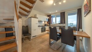 A modern kitchen with white cabinets, a dining area with a table and chairs, and a staircase with wooden steps. - exklusives Appartement in Rechlin (Rechlin)