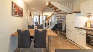 A modern kitchen with white cabinets, a wooden dining table, and black chairs. A staircase leads to an upper level. - exklusives Appartement in Rechlin (Rechlin)