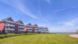A row of red and white multi-story buildings with balconies, a well-maintained lawn, and a clear view of the sea. - exklusives Appartement in Rechlin (Rechlin)