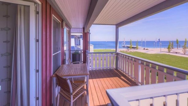 A wooden deck with a table and chairs, overlooking a beach with a clear view of the ocean and a few flags. - exklusives Appartement in Rechlin (Rechlin)