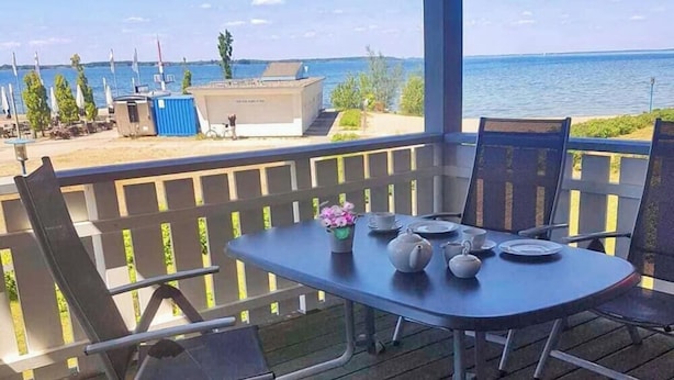 Un balcon avec une table dressée pour le dîner, offrant une vue sur une étendue d’eau et une côte lointaine.