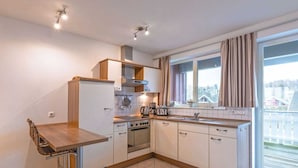 Une cuisine moderne avec des meubles blancs, un four encastré, une machine à café et une fenêtre avec des rideaux.