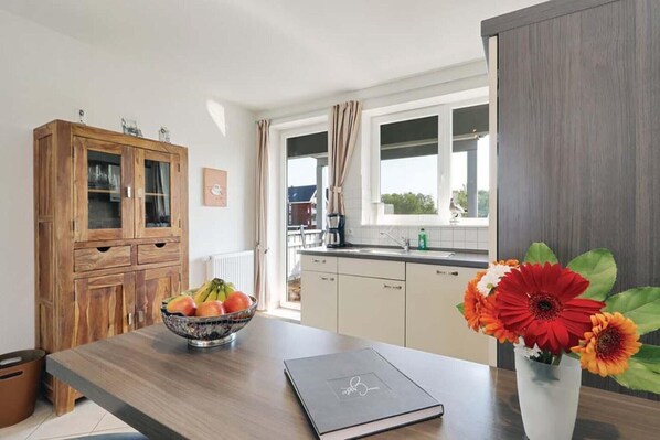 A modern kitchen with a wooden cabinet, a fruit bowl, a vase with flowers, and a book on the counter.