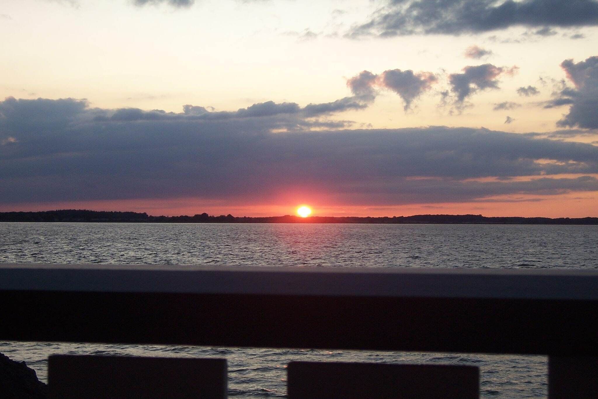 Een zonsondergang boven een wateroppervlak met een verre kustlijn.