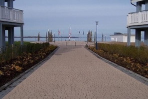 Ein gepflasterter Weg führt zu einer Uferpromenade, begleitet von zwei Gebäuden an jeder Seite.