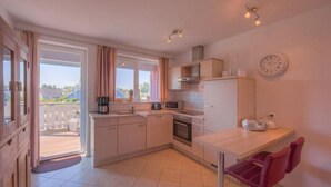 A compact kitchen with a dining area, a view through the window, and a clock on the wall. - Appartement im Ferienpark in Rechlin (Rechlin)