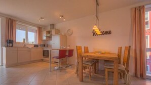 A modern kitchen with a dining area, a red chair, and a 'Welcome' sign on the wall. - Appartement im Ferienpark in Rechlin (Rechlin)