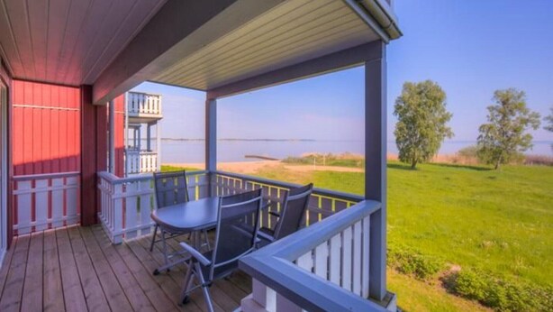 A wooden deck with a table and chairs, overlooking a grassy area and a body of water. - Appartement im Ferienpark in Rechlin (Rechlin)