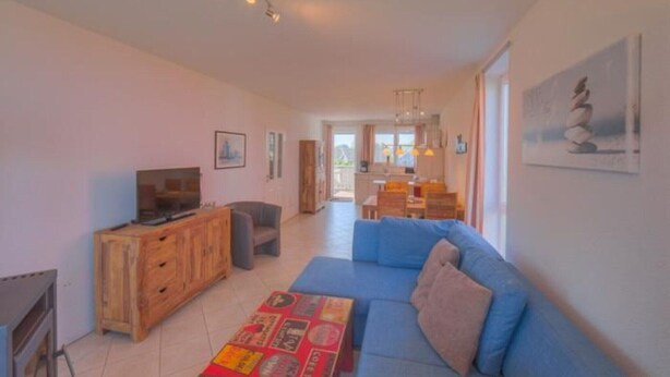 A spacious living area with a blue sofa, wooden entertainment unit, and a dining area in the background. - Appartement im Ferienpark in Rechlin (Rechlin)