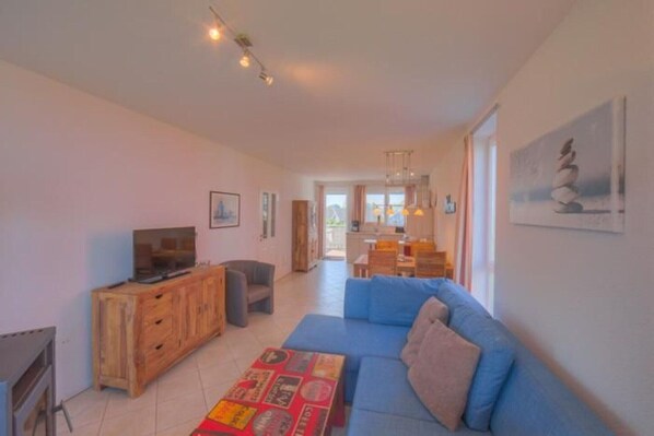 A spacious living area with a blue sofa, wooden entertainment unit, and a dining area in the background. - Appartement im Ferienpark in Rechlin (Rechlin)