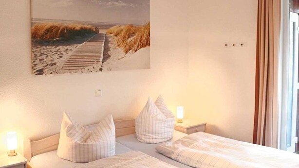 A hotel room with two beds, a painting of a beach scene, and a window with curtains. - liebevoll eingerichtetes Appartement (Rechlin)