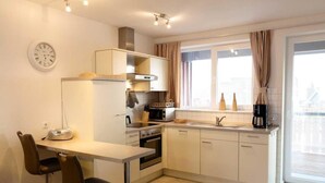 A compact kitchen with white cabinets, a stove, a microwave, a sink, and a window with curtains. - liebevoll eingerichtetes Appartement (Rechlin)