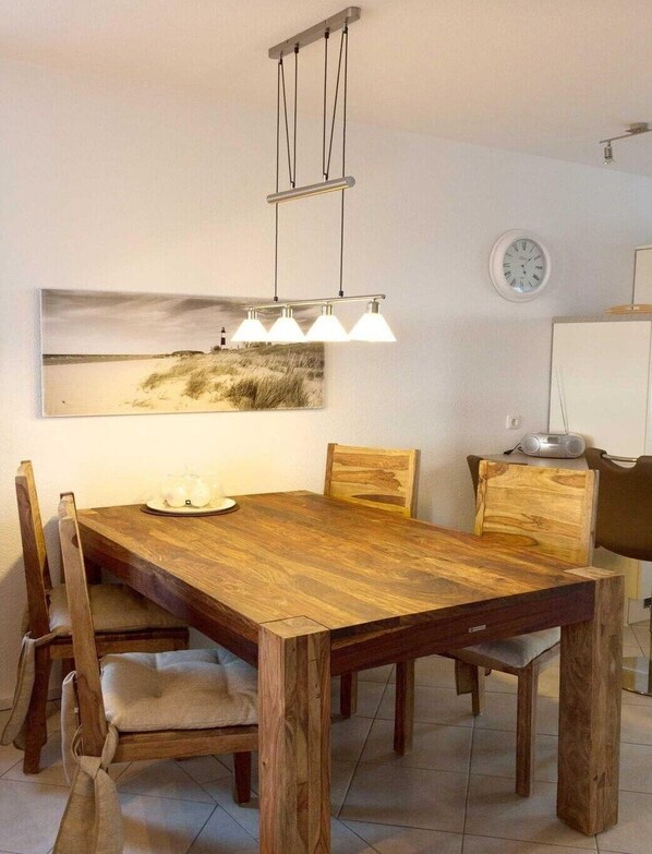 A dining area with a wooden table, four chairs, a hanging light fixture, and a wall-mounted clock.