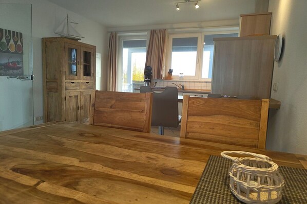 Una mesa de comedor de madera con sillas, una zona de cocina con ventana y un armario con un modelo de barco en la parte superior.