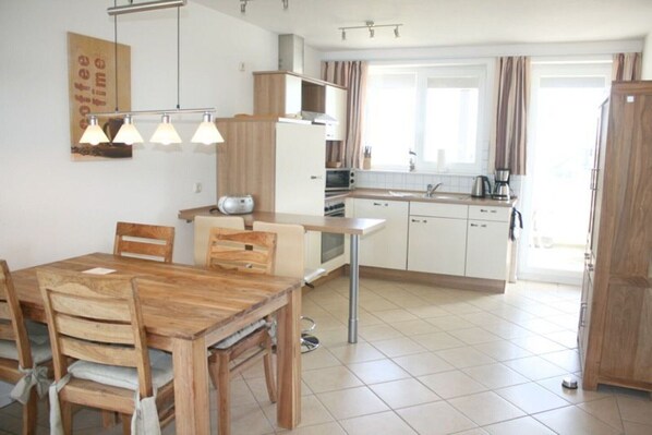 A modern kitchen with white cabinets, a wooden dining table, and a coffee machine. - liebevoll eingerichtetes Appartement (Rechlin)