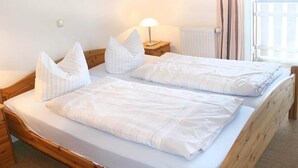 A double bed with white linens and pillows, a bedside table with a lamp, and a window with curtains. - liebevoll eingerichtetes Appartement (Rechlin)