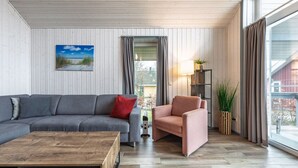 Ett modernt vardagsrum med en grå soffa, en rosa fåtölj, ett träbord och ett stort fönster med gardiner.