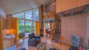 A spacious living area with a fireplace, comfortable seating, a staircase, and large windows offering a view of the outdoors. - Ferienhaus im skandinavischen Stil (Granzow)