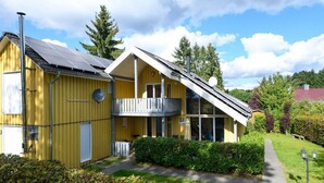 A yellow building with a balcony, solar panels, and a pathway leading to the entrance. - Ferienhaus im skandinavischen Stil (Granzow)