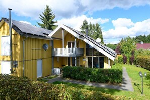 A yellow building with a balcony, solar panels, and a pathway leading to the entrance. - Ferienhaus im skandinavischen Stil (Granzow)